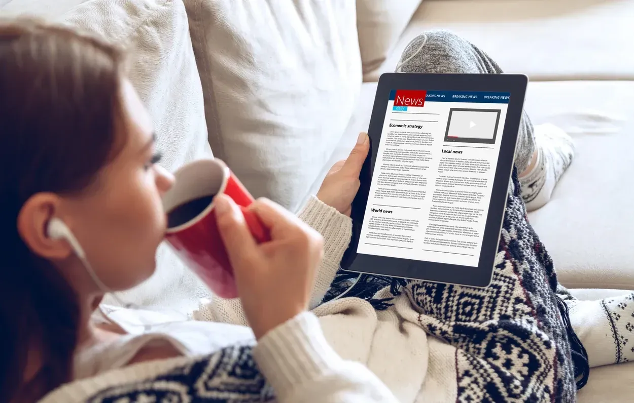 A reader with a cup of coffee reading a news portal on a tablet