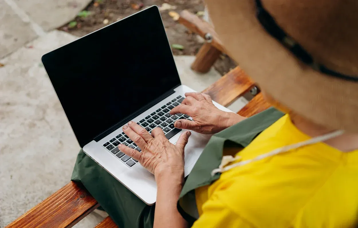 Gošća sa šeširom rezerviše turu na laptopu, na klupi na otvorenom
